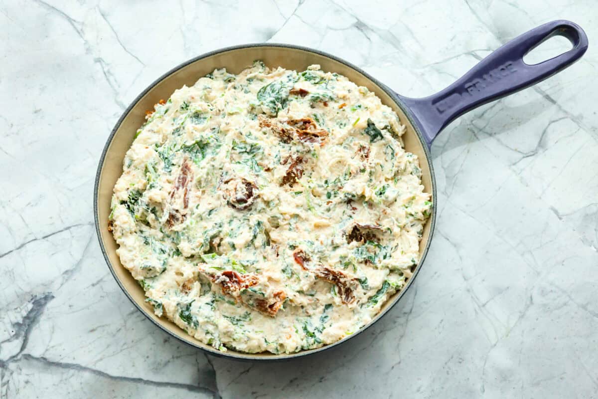 There's a new appetizer in town, and this creamy Tuscan dip won everyone's hearts! The combination of cheeses, garlic, spinach, and sun-dried tomatoes creates an addicting dip you’ll want to bring to all of your gatherings! Fourth photo of the dip spread into a skillet before baking.