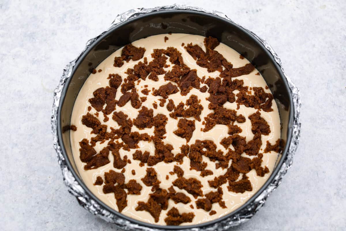 Rich and creamy Cinnamon Roll Cheesecake has the delicious flavor of a cinnamon roll in decadent cheesecake form. This irresistible dessert is made with a cinnamon graham cracker crust, a velvety cream cheese filling with spiced cinnamon throughout, and a classic whipped cream topping. Overhead shot of cream cheese filling with bits of cinnamon sugar mixtures over the top in the springform pan.