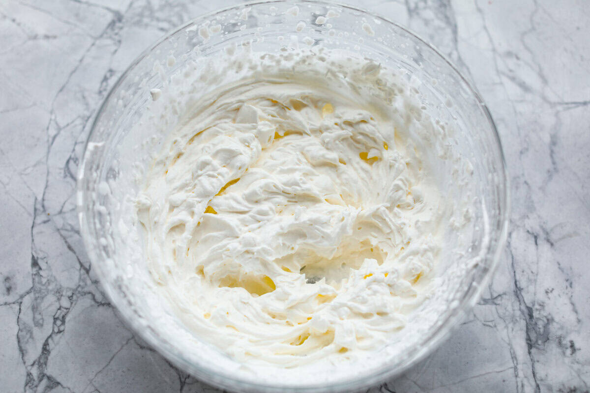 Rich and creamy Cinnamon Roll Cheesecake has the delicious flavor of a cinnamon roll in decadent cheesecake form. This irresistible dessert is made with a cinnamon graham cracker crust, a velvety cream cheese filling with spiced cinnamon throughout, and a classic whipped cream topping. Overhead shot of whipped whipped cream.