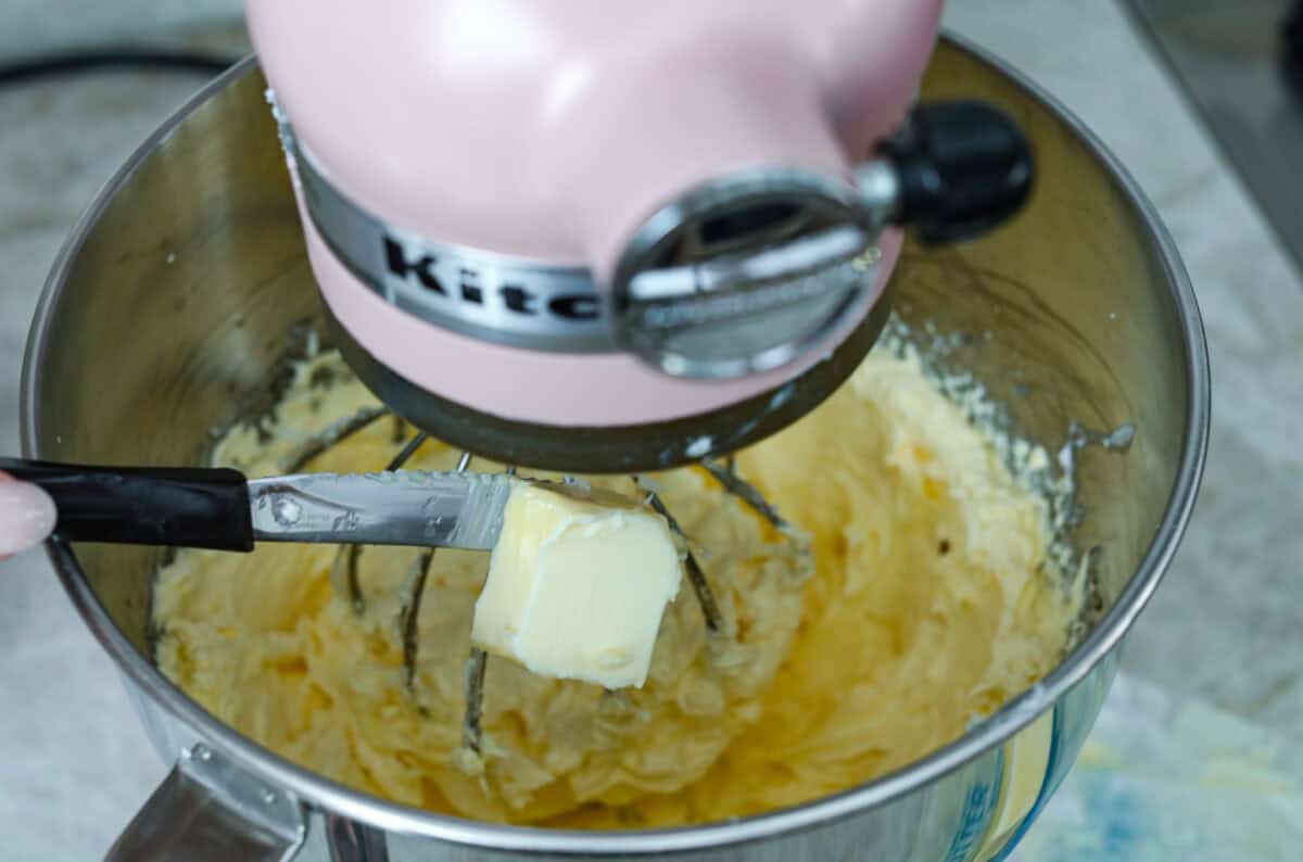 French buttercream is a luxurious, creamy frosting that will wow your guests and tantalize your taste buds. The elegant flavor comes from using egg yolks as the base and delicious, simple syrup for sweetness. Elevate your baking game with this unique recipe. Tablespoon of butter being dropped into a stand mixer that is mixing french buttercream.
