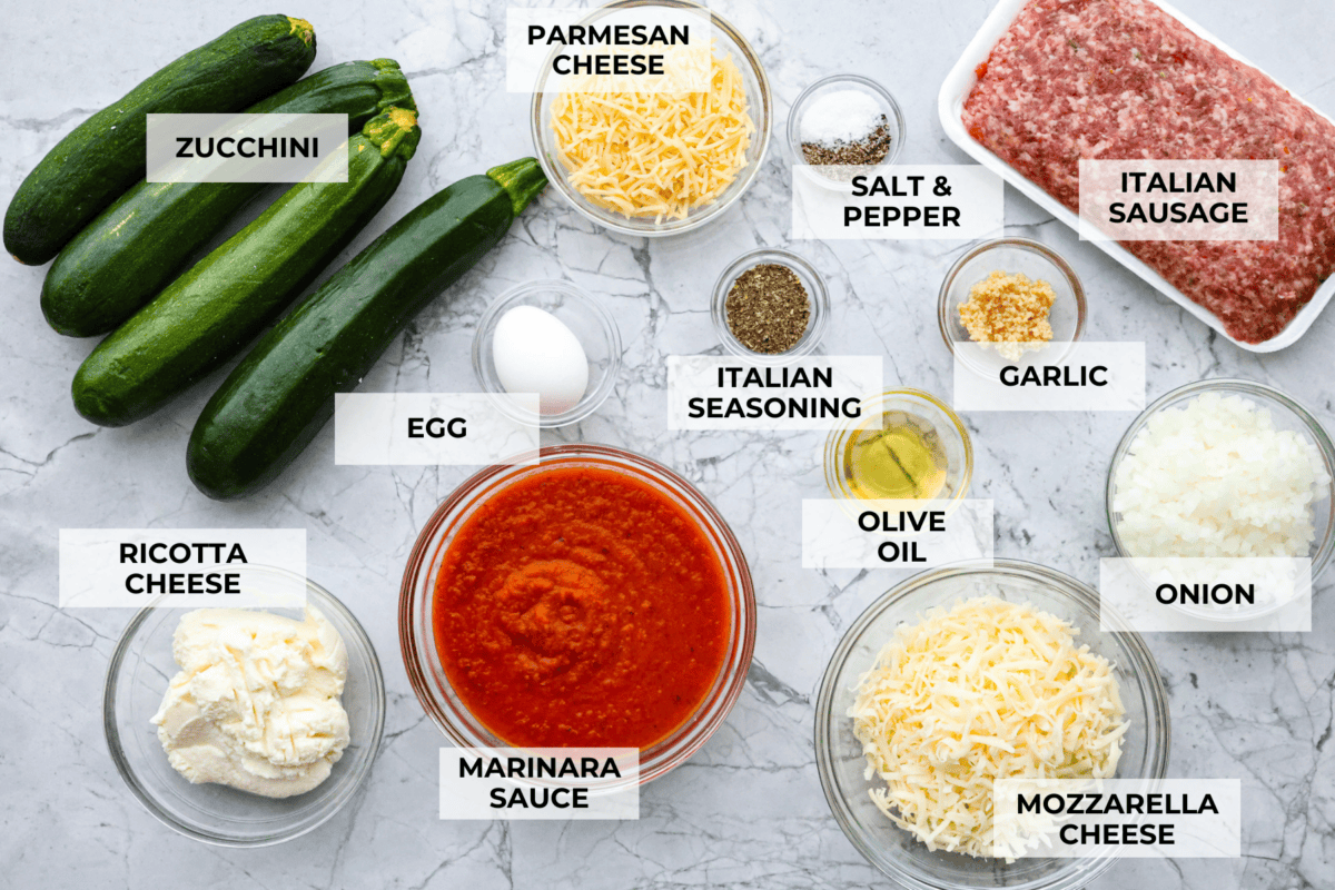 Zucchini Roll-Ups are a delicious, unique meal that the whole family will enjoy. Thin slices of zucchini are rolled around a tasty sausage ricotta mixture and layered over marinara before being topped with cheese and baked to bubbly perfection! Overhead shot of labeled ingredients.