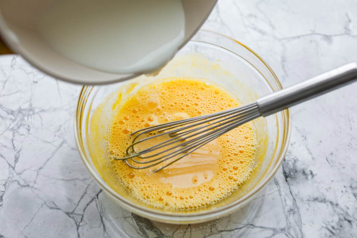 Decadent crème brûlée French toast is fluffy slices of brioche bread with a sweet golden crème brûlée topping. The creme anglaise sauce elevates the French toast making this an unforgettable breakfast! First photo of the steamed milk pouring into the sugar and eggs.