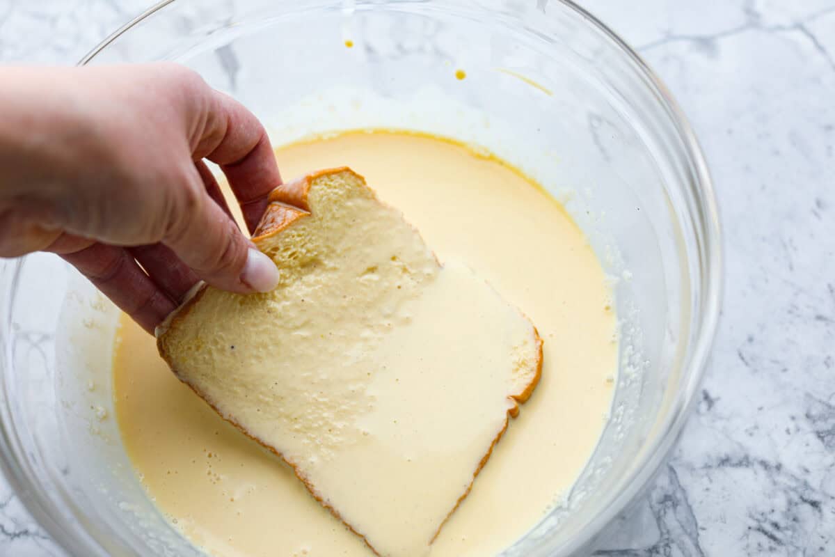 Decadent crème brûlée French toast is fluffy slices of brioche bread with a sweet golden crème brûlée topping. The creme anglaise sauce elevates the French toast making this an unforgettable breakfast! Fourth photo of the bread being dipped into the egg mixture.