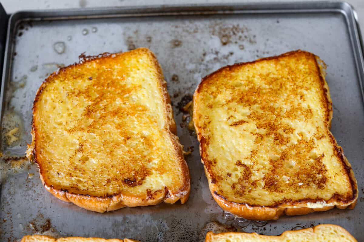 Decadent crème brûlée French toast is fluffy slices of brioche bread with a sweet golden crème brûlée topping. The creme anglaise sauce elevates the French toast making this an unforgettable breakfast! Fifth photo of the French toast cooking on the griddle.