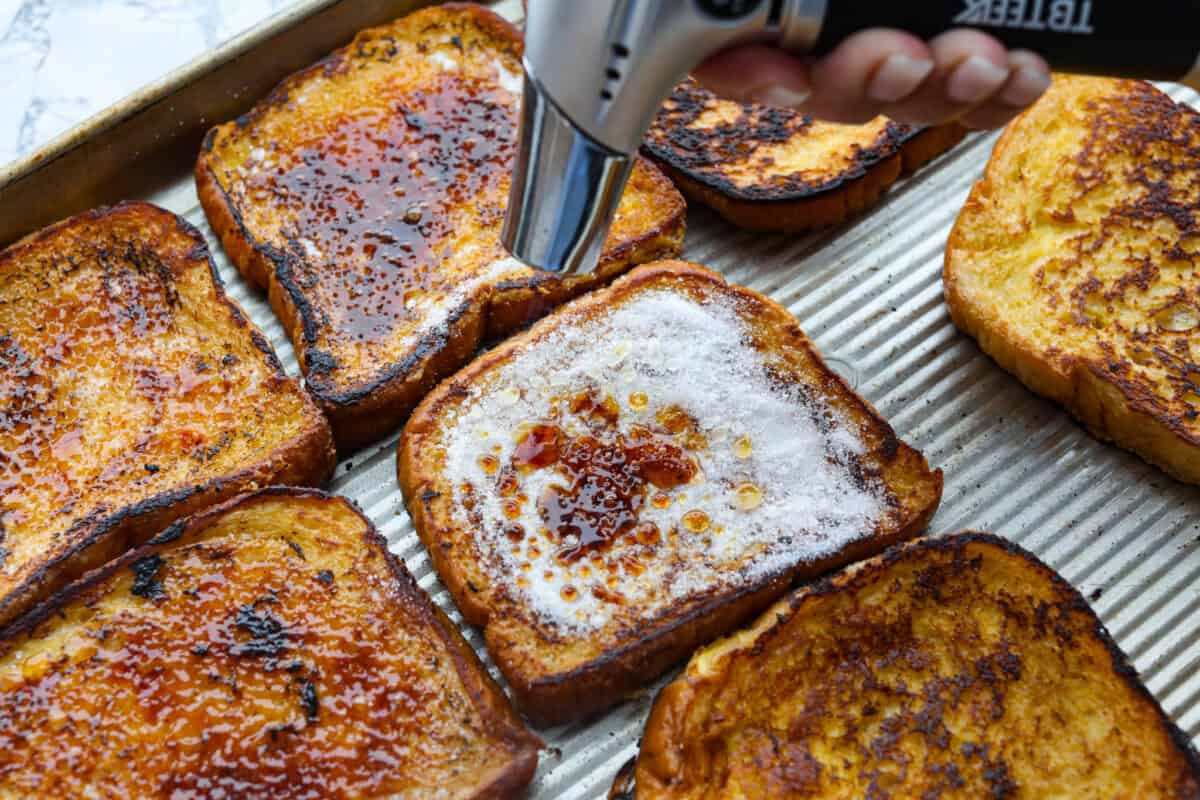 Decadent crème brûlée French toast is fluffy slices of brioche bread with a sweet golden crème brûlée topping. The creme anglaise sauce elevates the French toast making this an unforgettable breakfast! Sixth photo of the sugar being torched on top of the creme brûlée French toast.