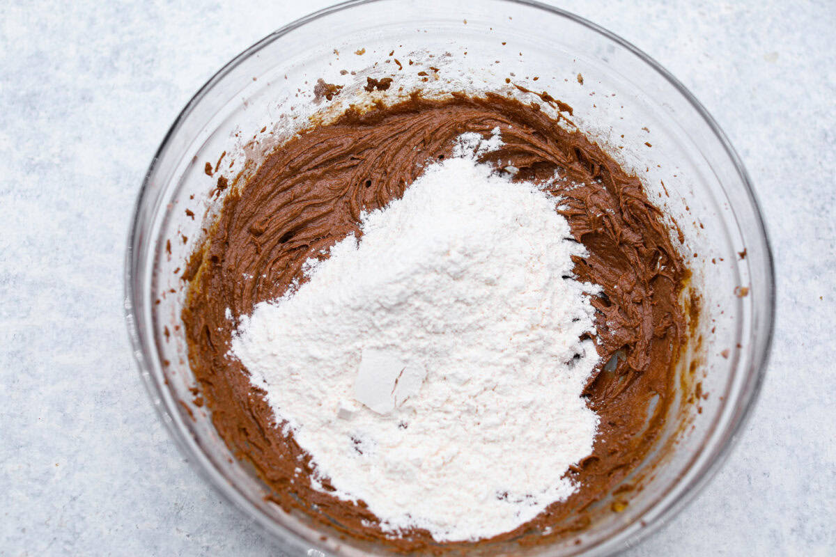 Chocolate Pudding Cookies are soft, chewy, and irresistibly delicious! They are quick and easy to bake and will be a huge hit with anyone who tries them! A bowl of chocolate pudding cookie dough with flour being added.