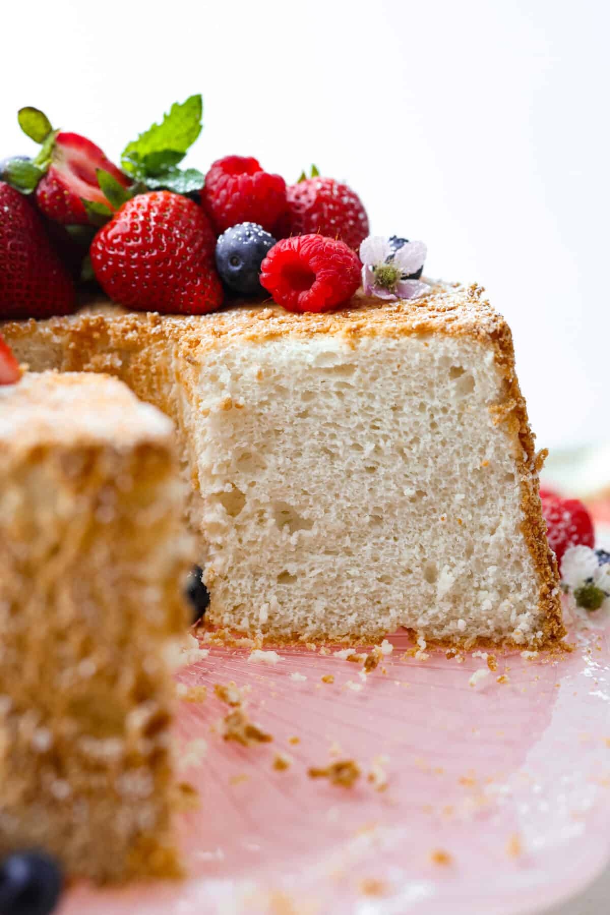 This light & fluffy Angel Food Cake is like a slice of heaven on a plate! It's delicious all on its own but absolutely divine topped with sweetened whipped cream and fresh berries or lemon curd! Side shot of angel food cake covered in berries with a slice taken out of it.
