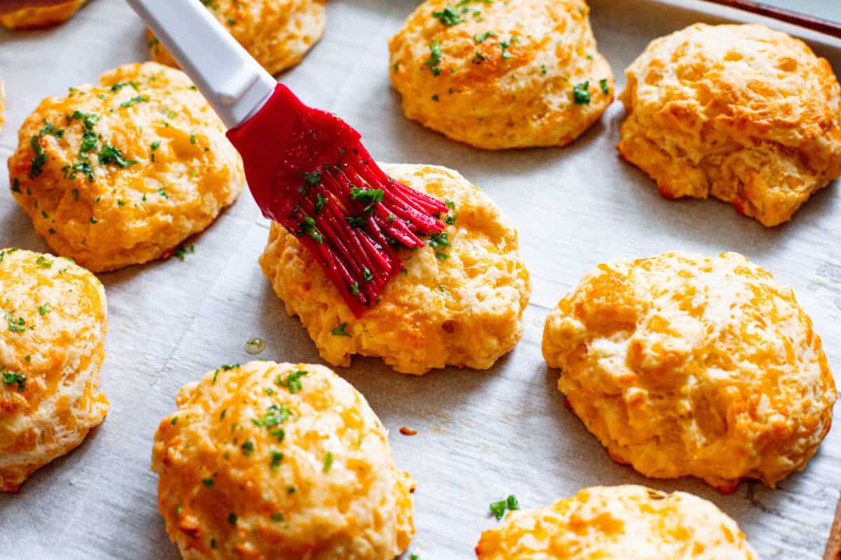 These delicious Copycat Red Lobster Cheddar Bay Biscuits are better than the real thing! Warm, buttery, and ready in 20 minutes! Fourth photo of the butter topping brushing on the red lobster cheddar bay biscuits.
