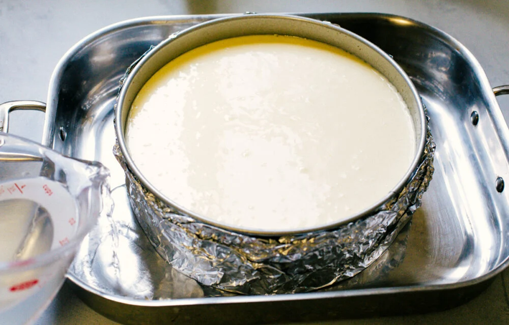 Cheesecake is my absolute FAVORITE dessert! I have perfected my method and I can't wait to teach you how to make cheesecake in this ultimate step-by-step guide. You're on your way to being a cheesecake-making pro! Water bath with water pouring into the roasting pan.