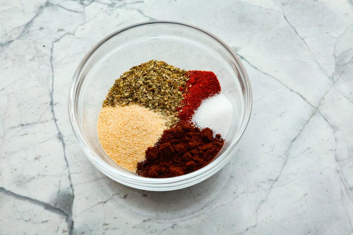 Enjoy a perfect blend of smoky and spicy flavors with this homemade Chipotle Seasoning! Featuring bold spices like chipotle powder, paprika, cumin, garlic powder, oregano, and more, this mix delivers a major flavor boost. Try it on everything from chicken to ground beef! Overhead shot of ingredients separated in a glass bowl.