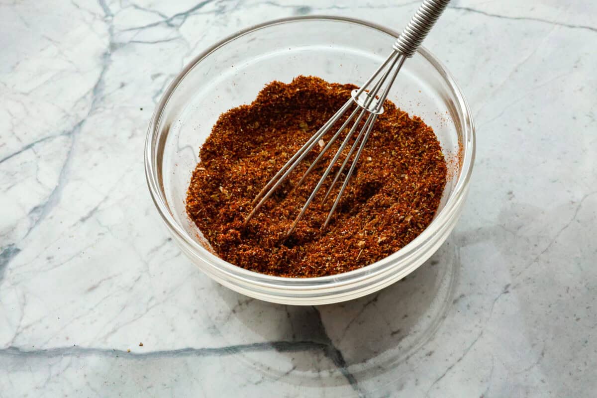 Enjoy a perfect blend of smoky and spicy flavors with this homemade Chipotle Seasoning! Featuring bold spices like chipotle powder, paprika, cumin, garlic powder, oregano, and more, this mix delivers a major flavor boost. Try it on everything from chicken to ground beef! Overhead shot of chipotle seasoning ingredients in a glass bowl with a whisk sticking out of it.