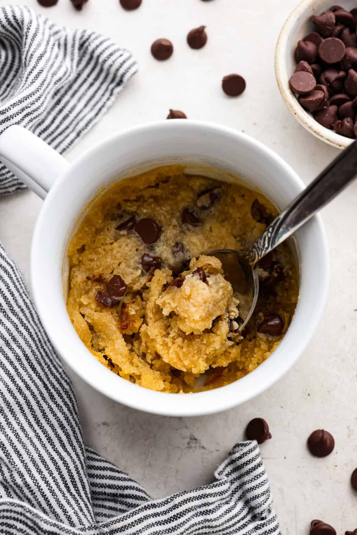 This cookie in a mug recipe is the perfect way to satisfy your cookie craving. In just a few minutes, you can enjoy a warm, buttery, ooey-gooey cookie right in your own mug. Top it with a scoop of ice cream or a dollop of whipped cream, and you'll find yourself in cookie heaven! Overhead shot of cookie in a mug with spoon.