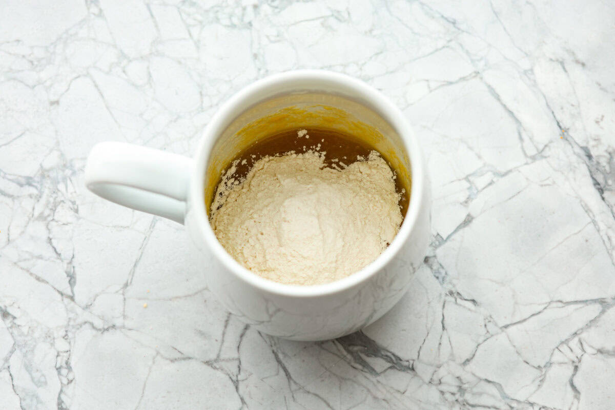 This cookie in a mug recipe is the perfect way to satisfy your cookie craving. In just a few minutes, you can enjoy a warm, buttery, ooey-gooey cookie right in your own mug. Top it with a scoop of ice cream or a dollop of whipped cream, and you'll find yourself in cookie heaven! Overhead shot of mug with flour and salt added to sugar, butter and egg mixture.