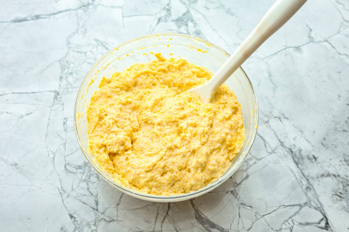 Cowboy Cornbread Casserole is a flavorful, comforting meal that's so easy to make. Seasoned ground beef, corn, pinto beans, and Rotel tomatoes are layered with shredded cheddar cheese and a cornbread topping for a winning dinner! Overhead shot of cornbread batter in glass bowl.