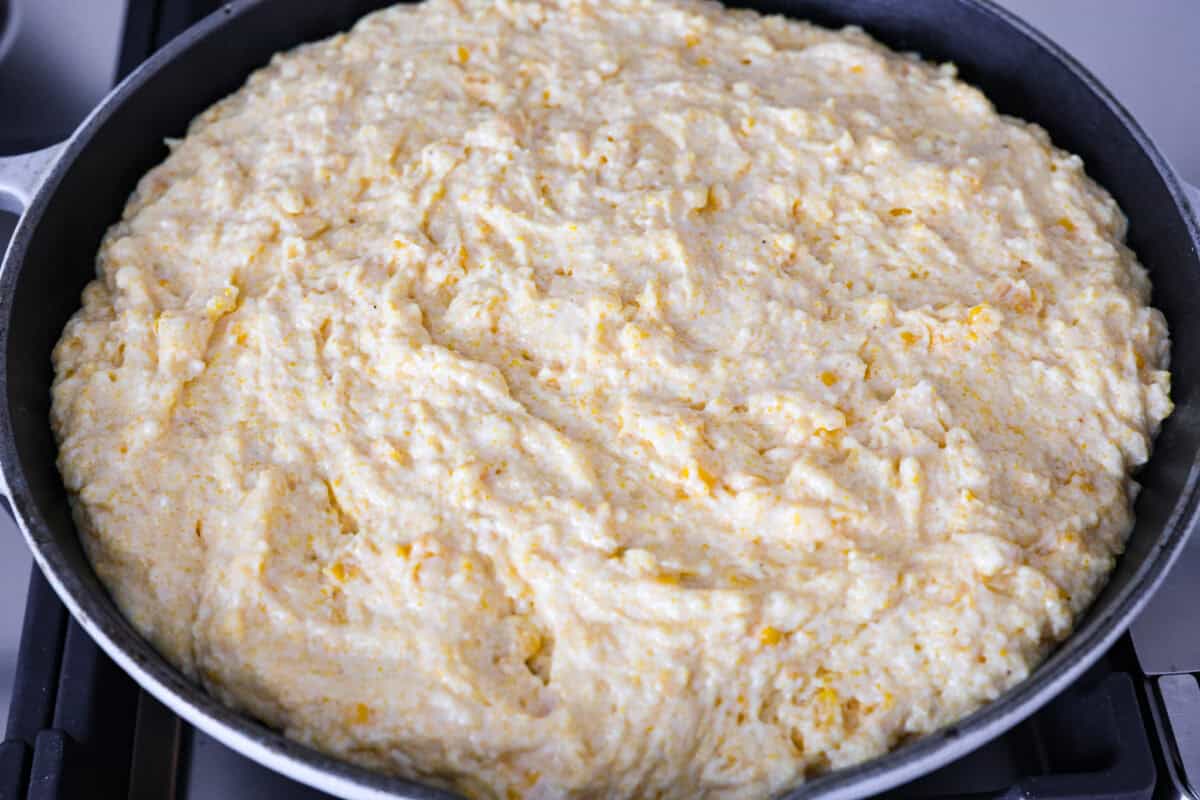 Cowboy Cornbread Casserole is a flavorful, comforting meal that's so easy to make. Seasoned ground beef, corn, pinto beans, and Rotel tomatoes are layered with shredded cheddar cheese and a cornbread topping for a winning dinner! Overhead shot of cornbread batter spread over ground beef and cheese mixture.