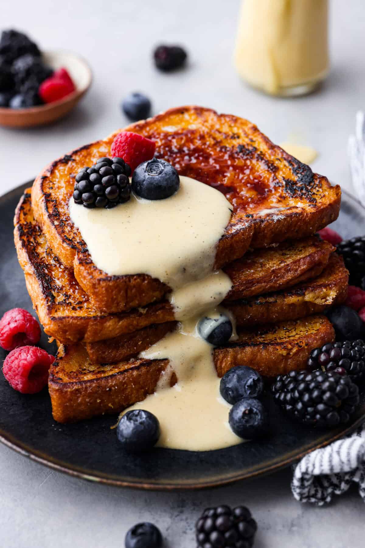 Decadent crème brûlée French toast is fluffy slices of brioche bread with a sweet golden crème brûlée topping. The creme anglaise sauce elevates the French toast making this an unforgettable breakfast! Close view of the stack French toast with creme anglaise sauce and berries on top.