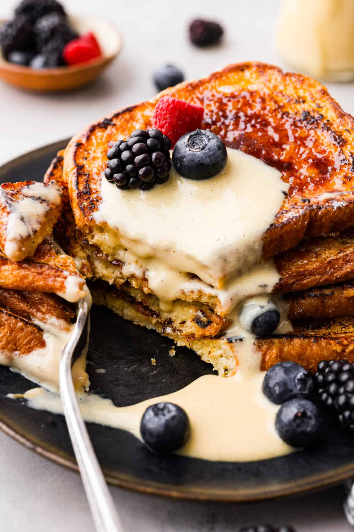 Decadent crème brûlée French toast is fluffy slices of brioche bread with a sweet golden crème brûlée topping. The creme anglaise sauce elevates the French toast making this an unforgettable breakfast! Close view of a fork cutting into the stacked creme brûlée French toast.