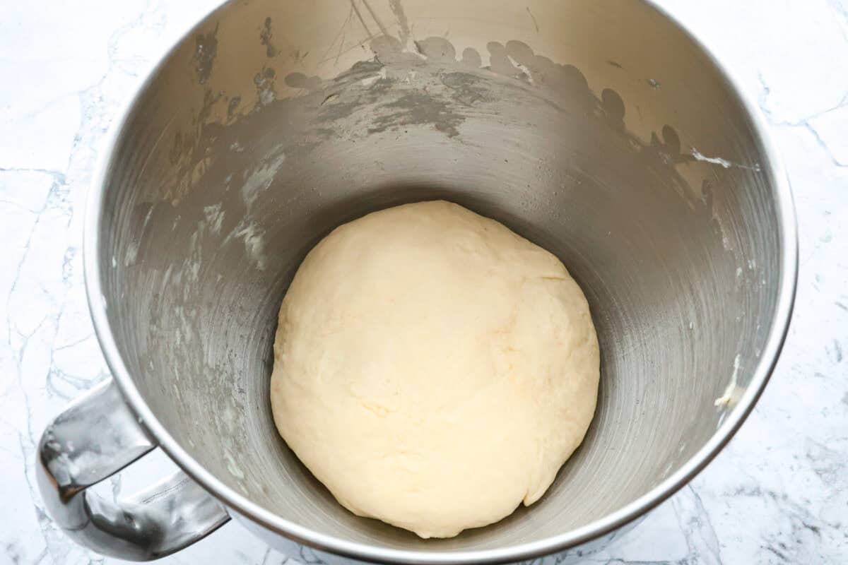 Croissant Bread is beautiful and fluffy with crispy, flaky layers on the outside. It's also one of the most delicious breads you'll ever taste - it will be love at first bite! Add it to your next brunch spread and use it to make French toast, sandwiches, and breakfast casseroles! Overhead shot of ball of croissant bread dough at the bottom of stand mixer bowl.