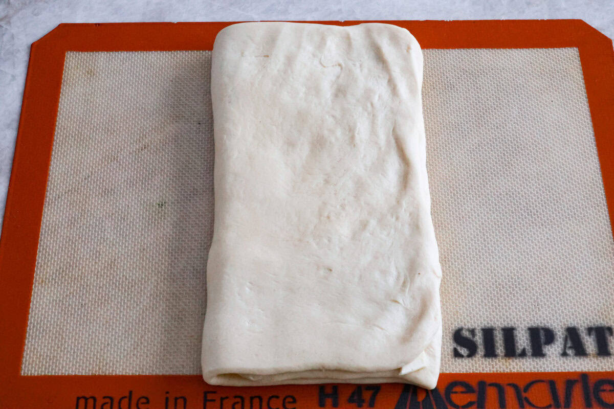 Croissant Bread is beautiful and fluffy with crispy, flaky layers on the outside. It's also one of the most delicious breads you'll ever taste - it will be love at first bite! Add it to your next brunch spread and use it to make French toast, sandwiches, and breakfast casseroles! Overhead shot of croissant bread dough folded in thirds.