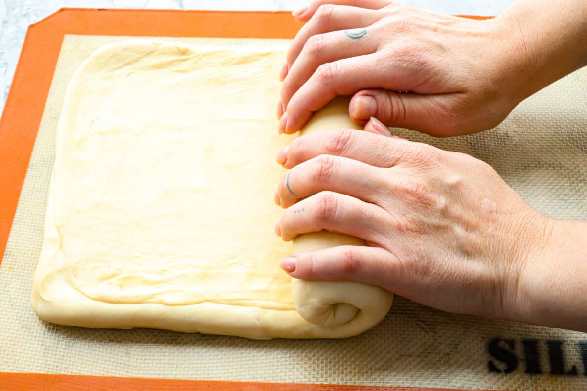 Croissant Bread is beautiful and fluffy with crispy, flaky layers on the outside. It's also one of the most delicious breads you'll ever taste - it will be love at first bite! Add it to your next brunch spread and use it to make French toast, sandwiches, and breakfast casseroles! Overhead shot of someone rolling up dough.