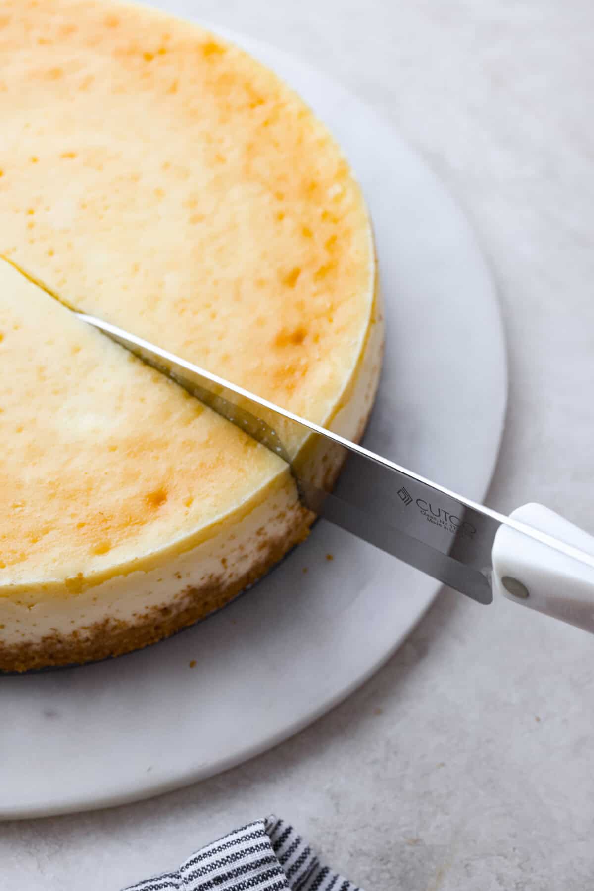 Cheesecake is my absolute FAVORITE dessert! I have perfected my method and I can't wait to teach you how to make cheesecake in this ultimate step-by-step guide. You're on your way to being a cheesecake-making pro! Second photo of a large knife cutting a slice of cheese.