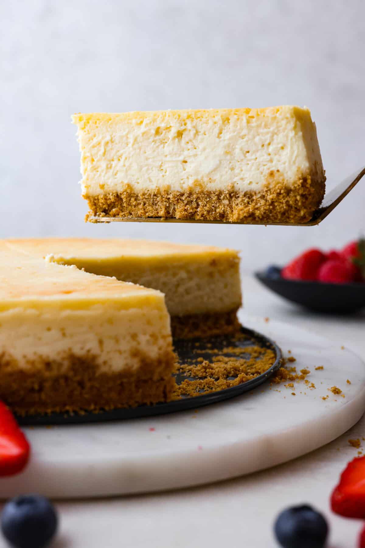 Cheesecake is my absolute FAVORITE dessert! I have perfected my method and I can't wait to teach you how to make cheesecake in this ultimate step-by-step guide. You're on your way to being a cheesecake-making pro! Close view of a slice of cheesecake lifting.