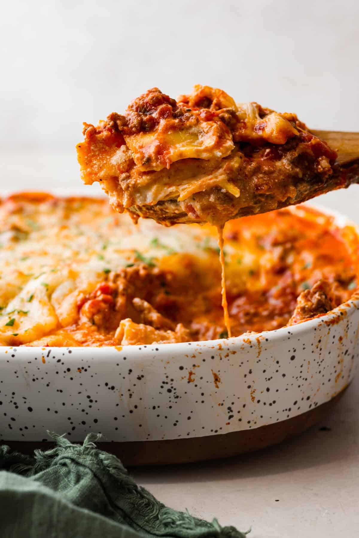 Million Dollar Ravioli Casseroleย is a flavorful casserole version of the classic! It's easy to make with mouthwatering layers of cheesy ravioli, meat sauce, and melted mozzarella cheese on top. This is a comforting, family-friendly dinner that you'll be craving on repeat! Side shot of a portion of million dollar ravioli casserole being scooped out of the baking dish.