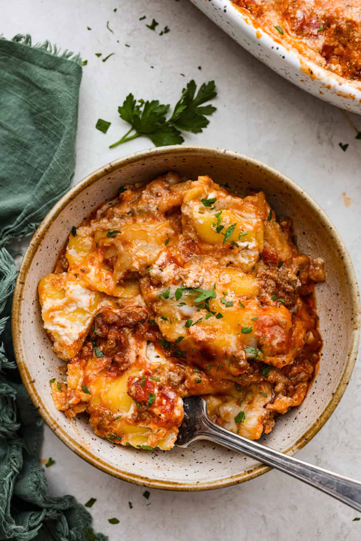 Million Dollar Ravioli Casseroleย is a flavorful casserole version of the classic! It's easy to make with mouthwatering layers of cheesy ravioli, meat sauce, and melted mozzarella cheese on top. This is a comforting, family-friendly dinner that you'll be craving on repeat! Overhead shot of a plated portion of million dollar ravioli casserole with a fork in it.