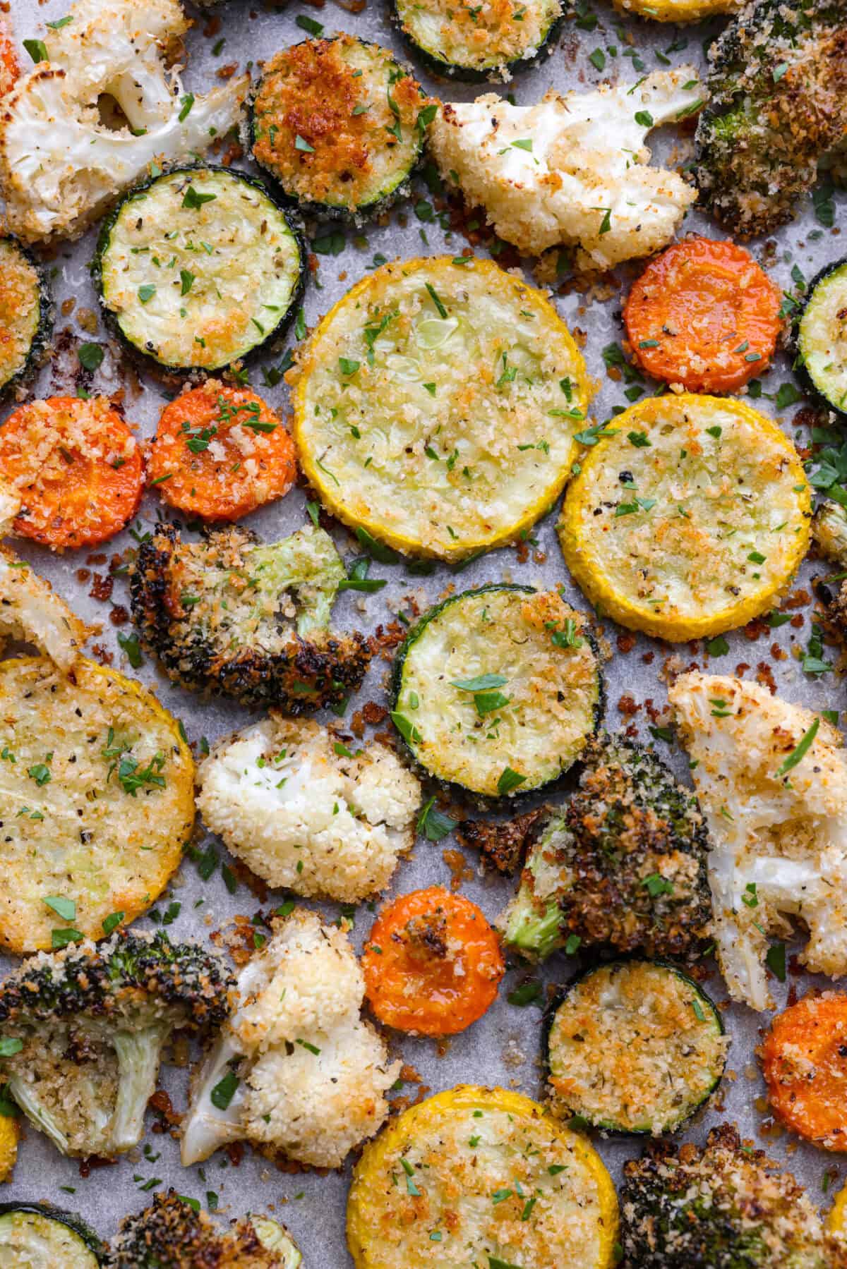 These delicious parmesan roasted vegetables are coated in zesty Italian dressing and a crispy parmesan mixture that delivers incredible flavor. This recipe cooks quickly and works with any vegetable you have on hand, whether using zucchini, cauliflower, or squash. Simply choose your favorite veggies! Close up shot of browned parmesan roasted vegetables.