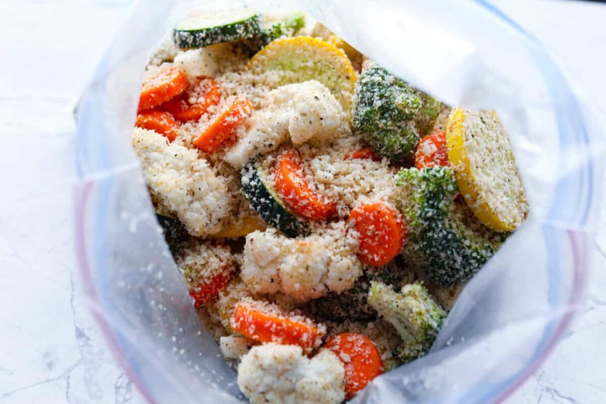These delicious parmesan roasted vegetables are coated in zesty Italian dressing and a crispy parmesan mixture that delivers incredible flavor. This recipe cooks quickly and works with any vegetable you have on hand, whether using zucchini, cauliflower, or squash. Simply choose your favorite veggies! Overhead shot of vegetables and breading in a ziplock bag.