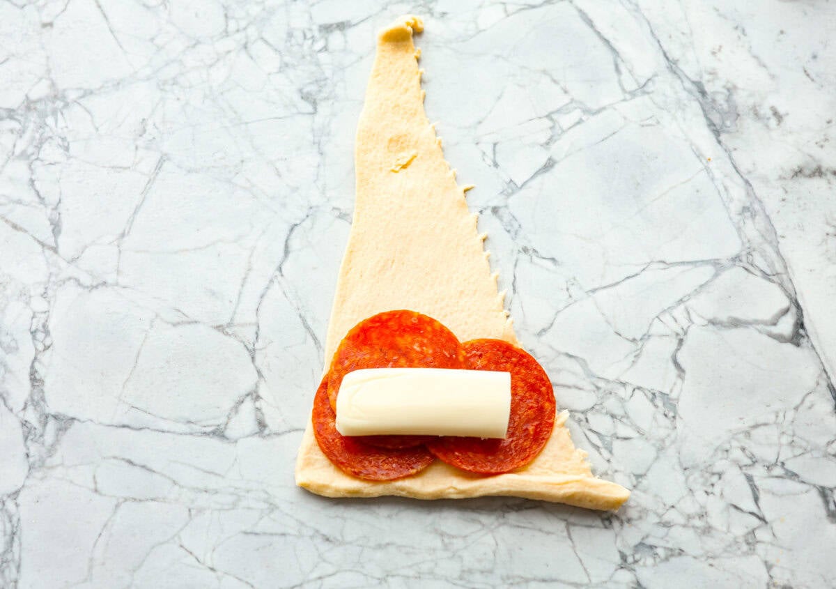 Pizza Stuffed Crescent Rolls areย loaded with gooey mozzarella cheese and pepperoni. Serve with warm marinara for dipping! Overhead shot of pepperoni and cheese stick on top of crescent triangle.