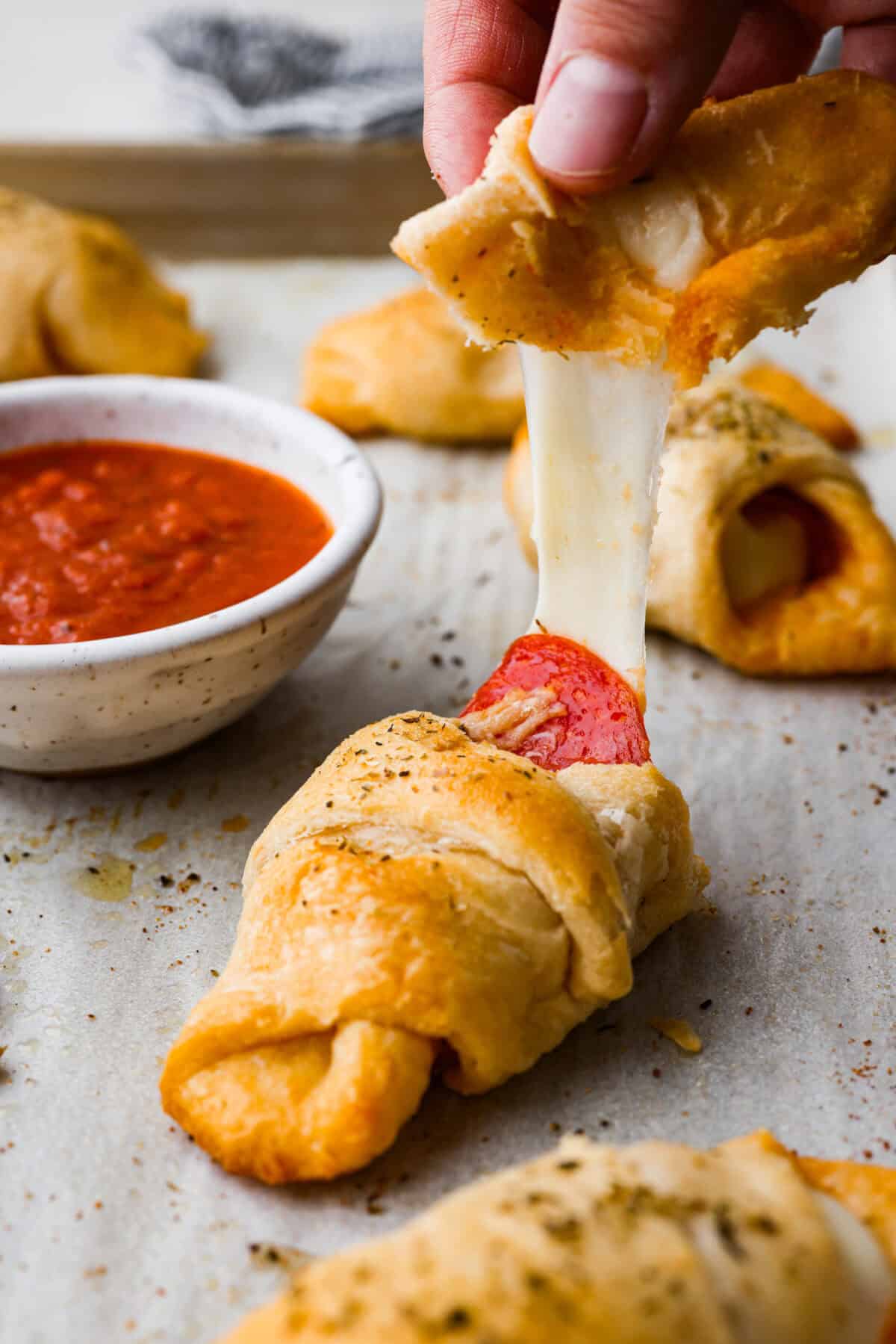 Pizza Stuffed Crescent Rolls areย loaded with gooey mozzarella cheese and pepperoni. Serve with warm marinara for dipping! Side shot of someone pulling apart a pizza stuffed crescent roll with a cheese pull.
