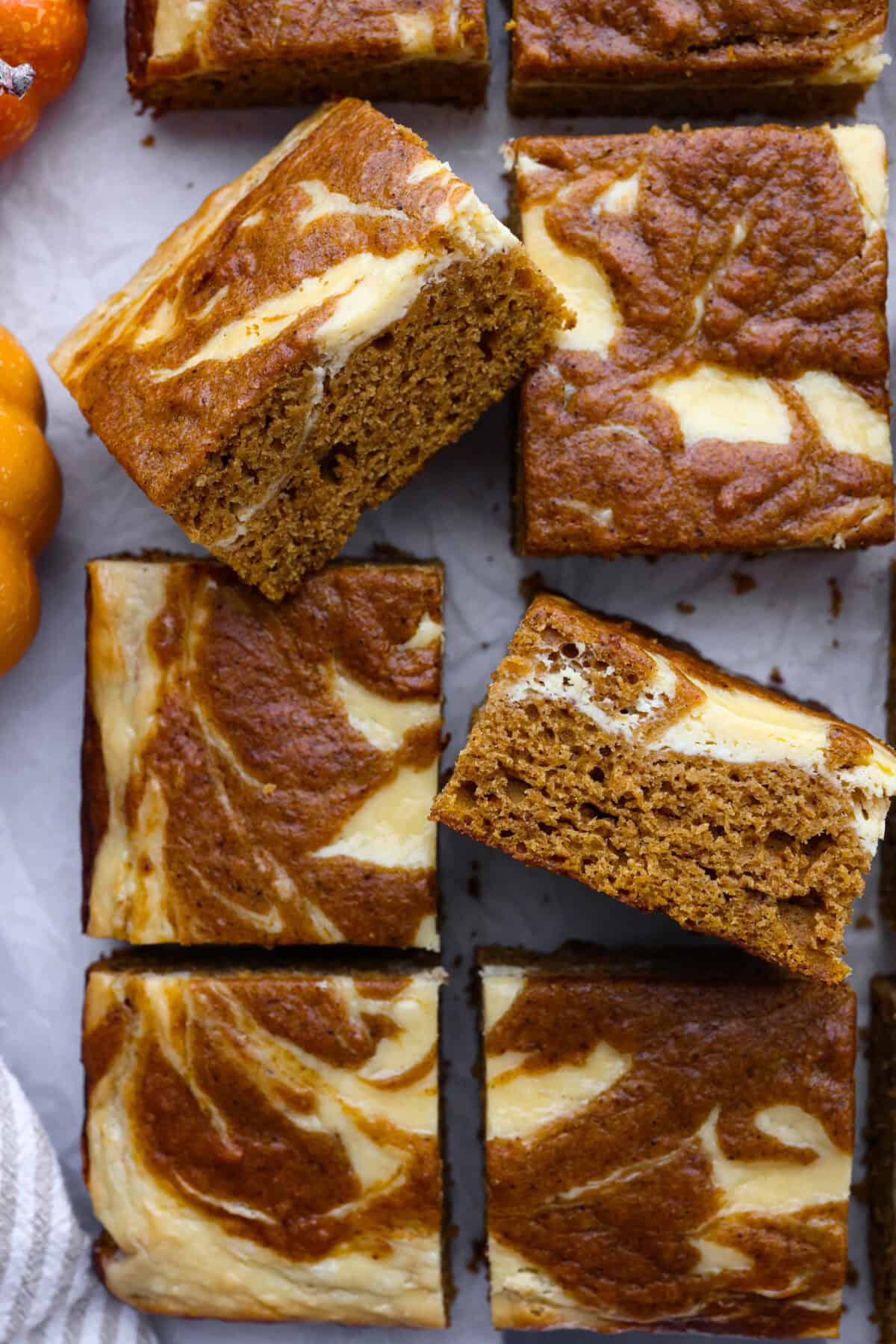 Pumpkin roll bars have all the things you love about pumpkin rolls without all of the hassle! They have perfectly spiced pumpkin cake with a smooth cream cheese swirl that will be sure to make this your new favorite fall dessert! Close up shot of pumpkin roll bars on parchment paper.