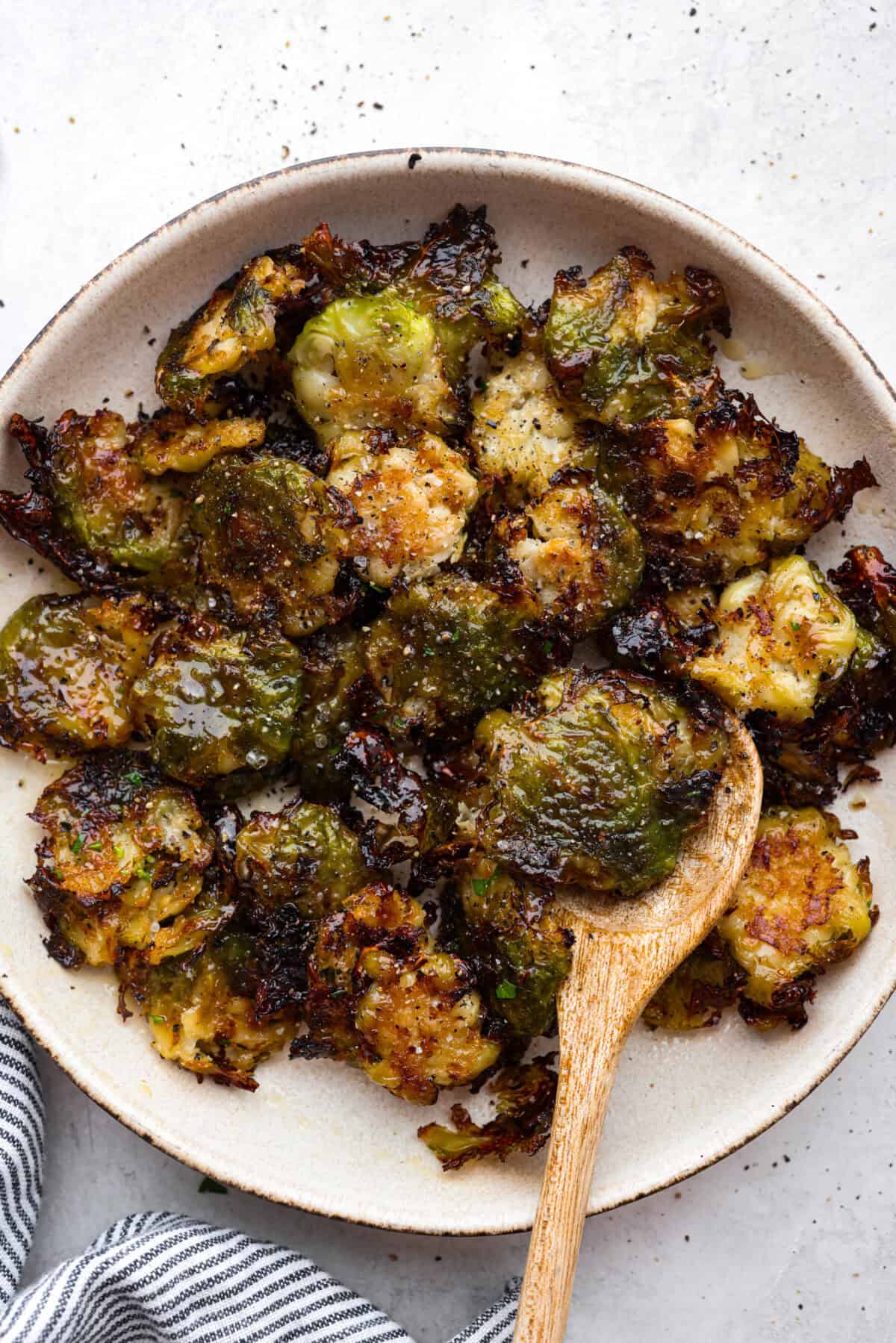 Irresistibly crispy Smashed Brussels Sprouts areย simple to make, loaded with delicious flavor, and have the best crunchy texture. These pair well with almost any protein and will definitely upgrade your side dish game! Overhead shot of smashed Brussels sprouts on a plate with a wooden serving spoon.