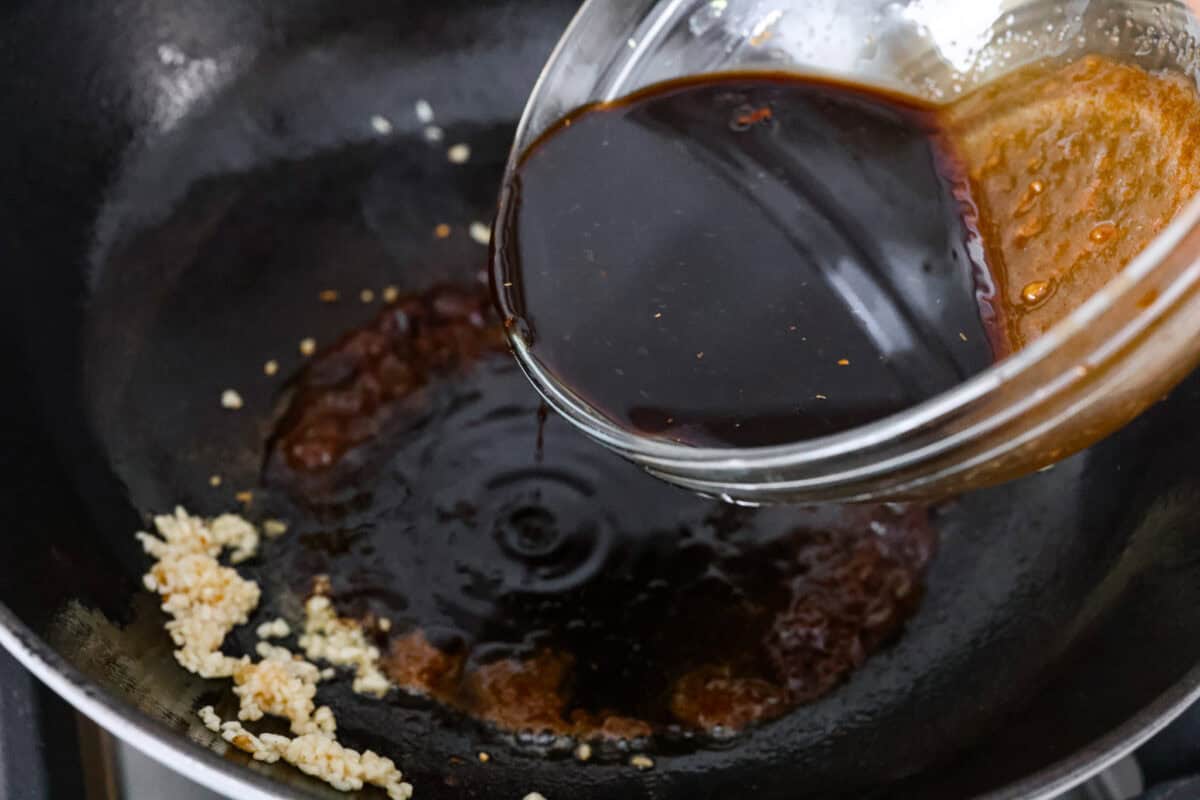Packed with flavor, these easy Teriyaki Noodles are so much better than takeout! Throw these together in just 20 minutes with pantry staples for the perfect busy weeknight dinner. You can keep it vegetarian or serve it alongside your favorite protein. Overhead shot of someone pouring teriyaki sauce into the skillet with oil and garlic.