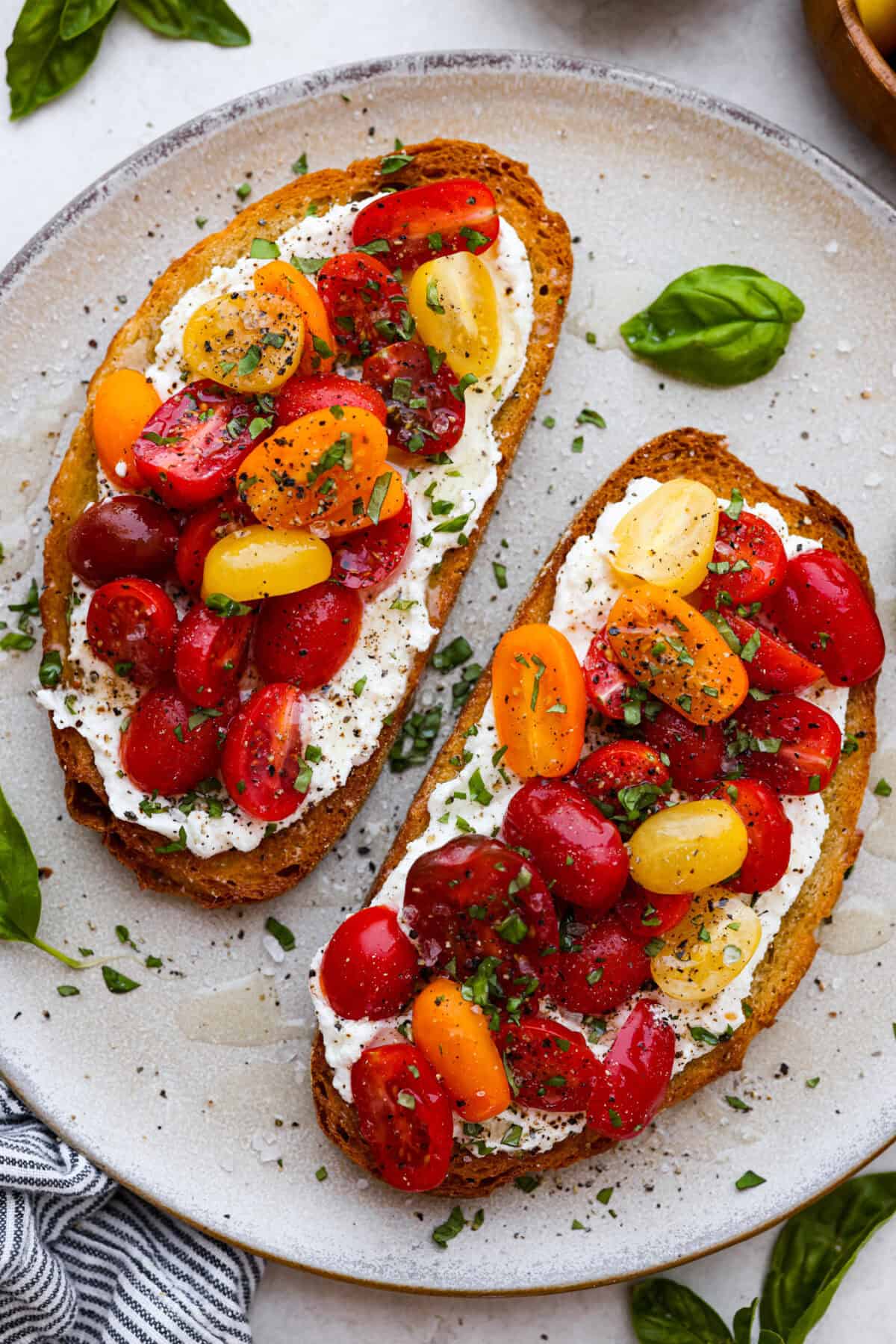Vibrantย Tomato Toastย has sweet, juicy tomatoes, garlic, creamy ricotta, and fresh basil layered on a crusty slice of toasted bread. Itโs delicious and savory with hints of sweetness. Serve it for breakfast, brunch, as an appetizer, or light lunch for the perfect way to use up summer produce. Overhead shot of plated tomato toast.