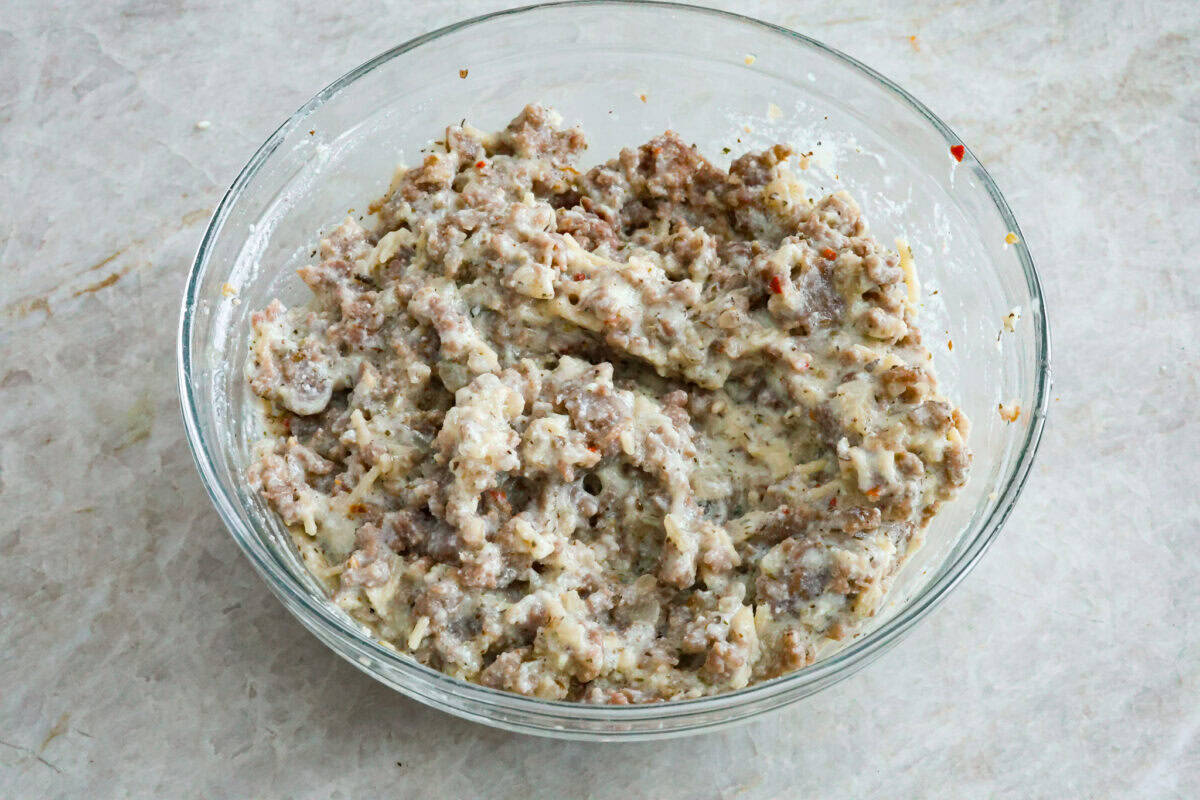 Zucchini Roll-Ups are a delicious, unique meal that the whole family will enjoy. Thin slices of zucchini are rolled around a tasty sausage ricotta mixture and layered over marinara before being topped with cheese and baked to bubbly perfection! Angle shot of cheese mixture combined with Italian sausage.