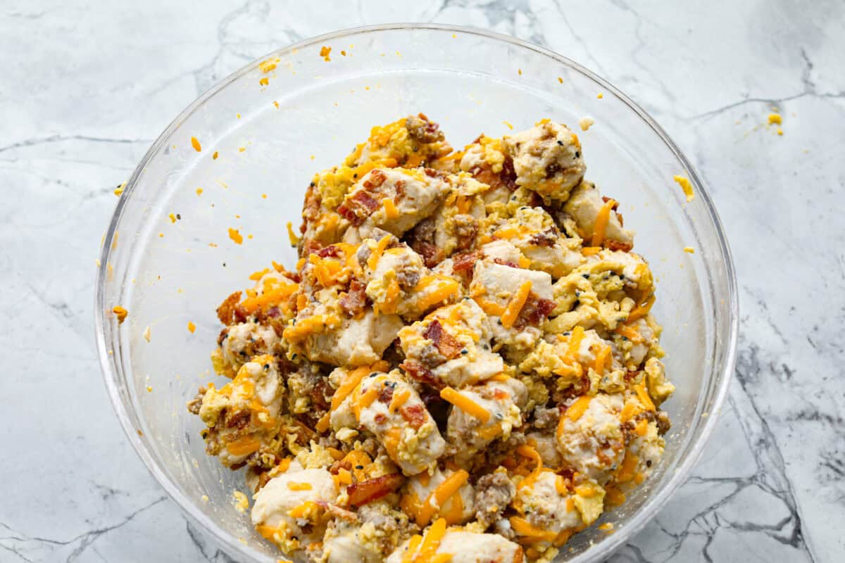 Rise and shine to Breakfast Monkey Bread with delicious savory flavors! It’s made with Grands biscuits, eggs, sausage, bacon, and cheese, all baked in a bundt pan. The result is crowd-pleasing pull-apart bread that everyone will devour! Overhead shot of breakfast monkey bread ingredients stirred together in a bowl.