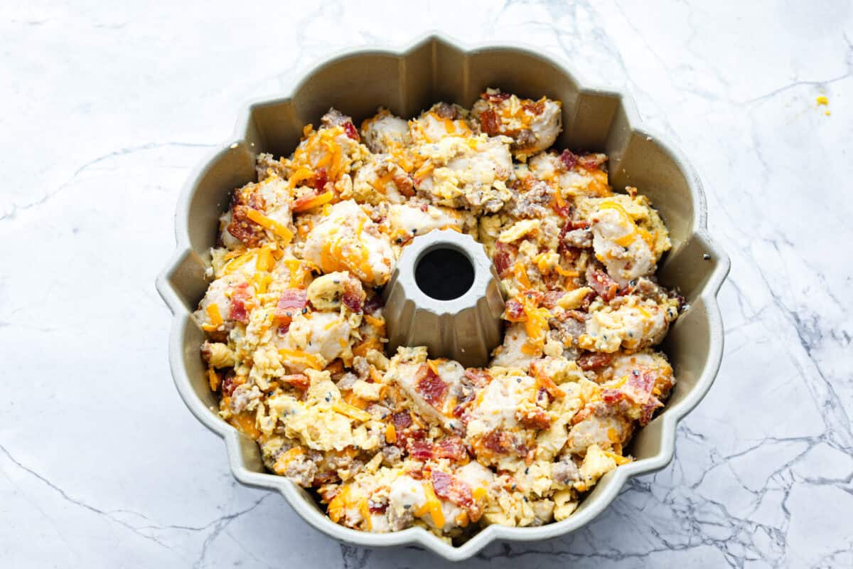Rise and shine to Breakfast Monkey Bread with delicious savory flavors! It’s made with Grands biscuits, eggs, sausage, bacon, and cheese, all baked in a bundt pan. The result is crowd-pleasing pull-apart bread that everyone will devour! Overhead shot of egg, cheese, meat and biscuit mixture in a bundt pan.