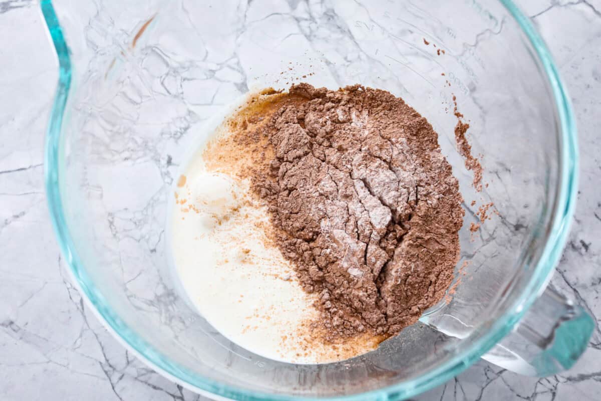 Fluffy Chocolate Whipped Cream is a wonderful combination of chocolate with fresh whipped cream! Itโs the perfect topping for fruit, waffles, pie, cupcakes and so much more! Overhead shot of dry ingredients with cream in a glass bowl.