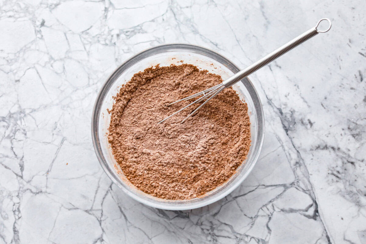 Fluffy Chocolate Whipped Cream is a wonderful combination of chocolate with fresh whipped cream! Itโs the perfect topping for fruit, waffles, pie, cupcakes and so much more! Overhead shot of dry ingredients in a glass bowl with a whisk.