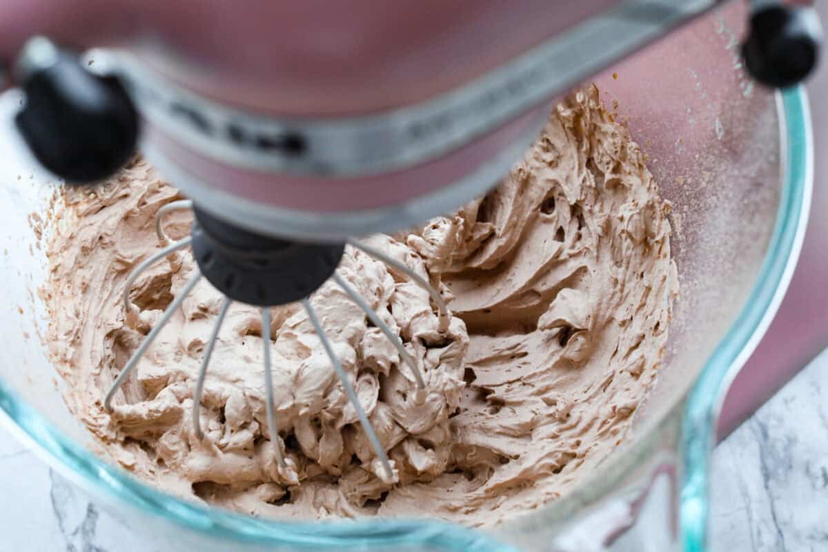 Fluffy Chocolate Whipped Cream is a wonderful combination of chocolate with fresh whipped cream! Itโs the perfect topping for fruit, waffles, pie, cupcakes and so much more! Overhead shot of chocolate whipped cream in stand mixer.