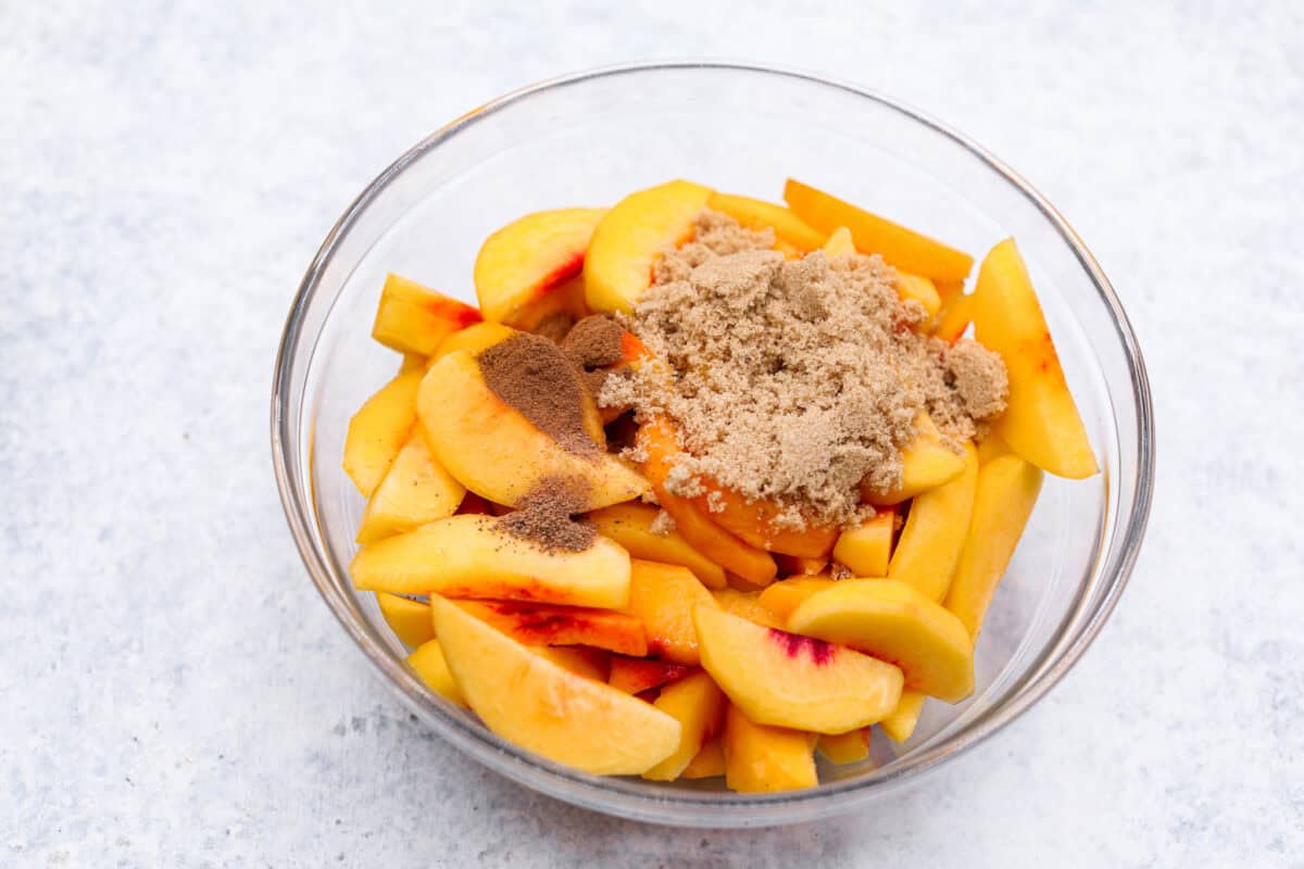 Enjoy juicy, ripe peaches in this Fresh Peach Pie. It has a creamy cheesecake filling topped with sweet peaches, all nestled in a buttery graham cracker crust. Itโs simply delightful, and no baking is required! Overhead shot of a bowl of sliced peaches with brown sugar, cinnamon and nutmeg on top.