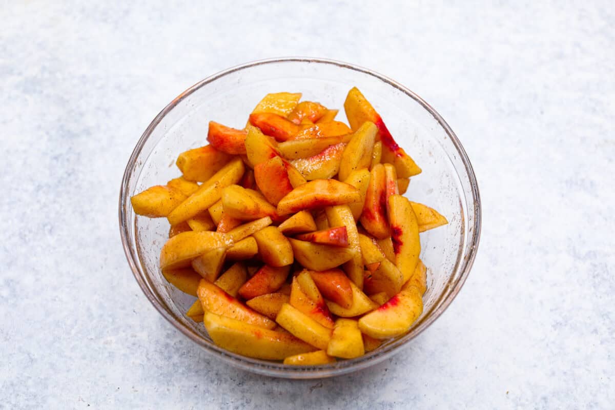 Enjoy juicy, ripe peaches in this Fresh Peach Pie. It has a creamy cheesecake filling topped with sweet peaches, all nestled in a buttery graham cracker crust. Itโs simply delightful, and no baking is required! Overhead shot of the brown sugar, cinnamon, and nutmeg mixed in with the peaches in a glass bowl.