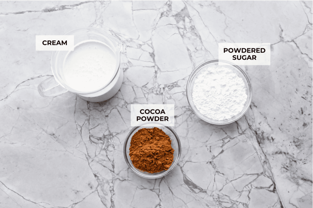Fluffy Chocolate Whipped Cream is a wonderful combination of chocolate with fresh whipped cream! Itโs the perfect topping for fruit, waffles, pie, cupcakes and so much more! Overhead shot of labeled ingredients.