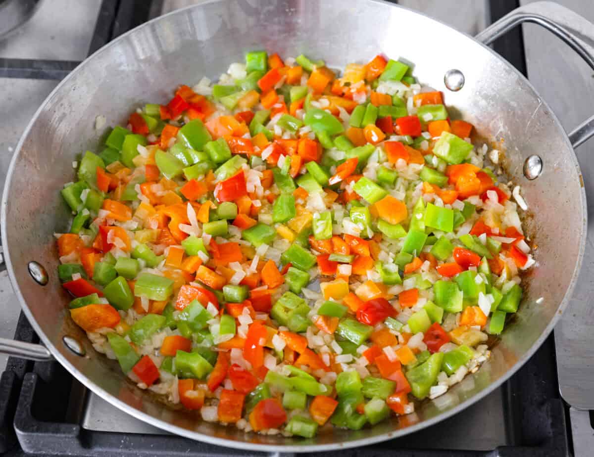 This delicious Louisiana Casserole has become an instant favorite in our house! It has all of the delicious flavors of a jambalaya in an easy-to-make casserole. Tasty andouille sausage, shrimp, veggies, rice and cajun seasoning come together for a complete meal on the table in just 40 minutes! Overhead shot of vegetables being sautรฉed in butter in a skillet.