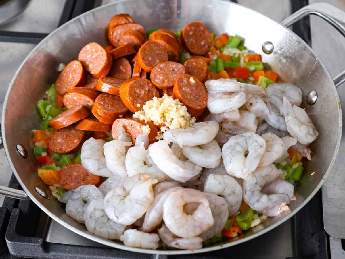 This delicious Louisiana Casserole has become an instant favorite in our house! It has all of the delicious flavors of a jambalaya in an easy-to-make casserole. Tasty andouille sausage, shrimp, veggies, rice and cajun seasoning come together for a complete meal on the table in just 40 minutes! Overhead shot of sausage and shrimp added to the sautรฉing veggies in a skillet.
