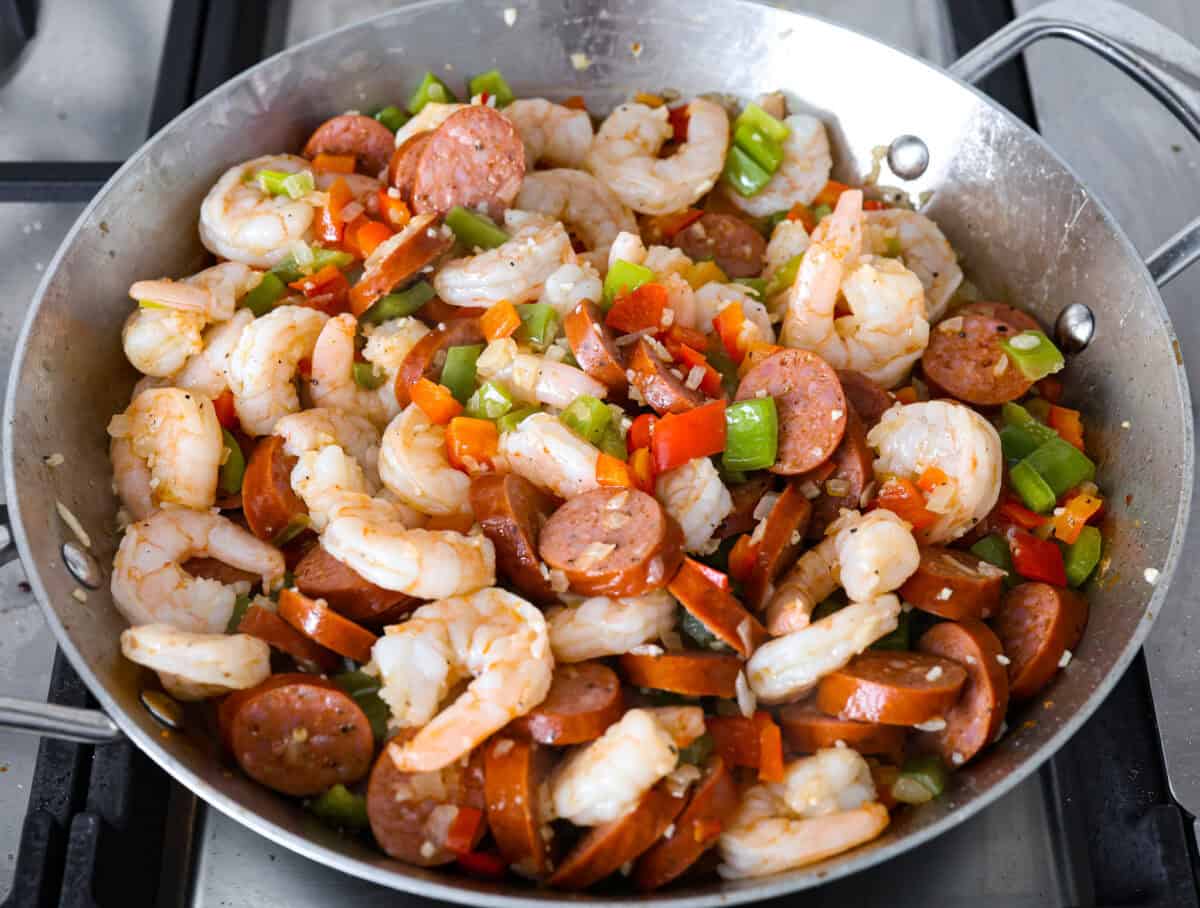 This delicious Louisiana Casserole has become an instant favorite in our house! It has all of the delicious flavors of a jambalaya in an easy-to-make casserole. Tasty andouille sausage, shrimp, veggies, rice and cajun seasoning come together for a complete meal on the table in just 40 minutes! Overhead shot of the shrimp, sausage and vegetables cooking in the skillet.