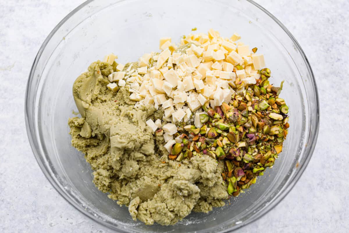 Pistachio Pudding Cookies are super soft, chewy, and irresistible! They're easy to make, and adding pistachio pudding mix gives this cookie recipe wonderful flavor and the perfect tender texture! Overhead shot of the pistachio pudding cookie dough with white chocolate chunks and pistachios in a mixing bowl.