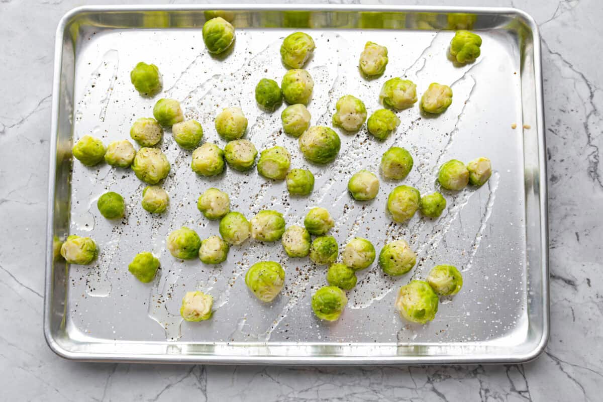 Irresistibly crispy Smashed Brussels Sprouts areย simple to make, loaded with delicious flavor, and have the best crunchy texture. These pair well with almost any protein and will definitely upgrade your side dish game! Overhead shot of boiled Brussels sprouts on a baking sheet drizzled with oil and sprinkled with salt and pepper.